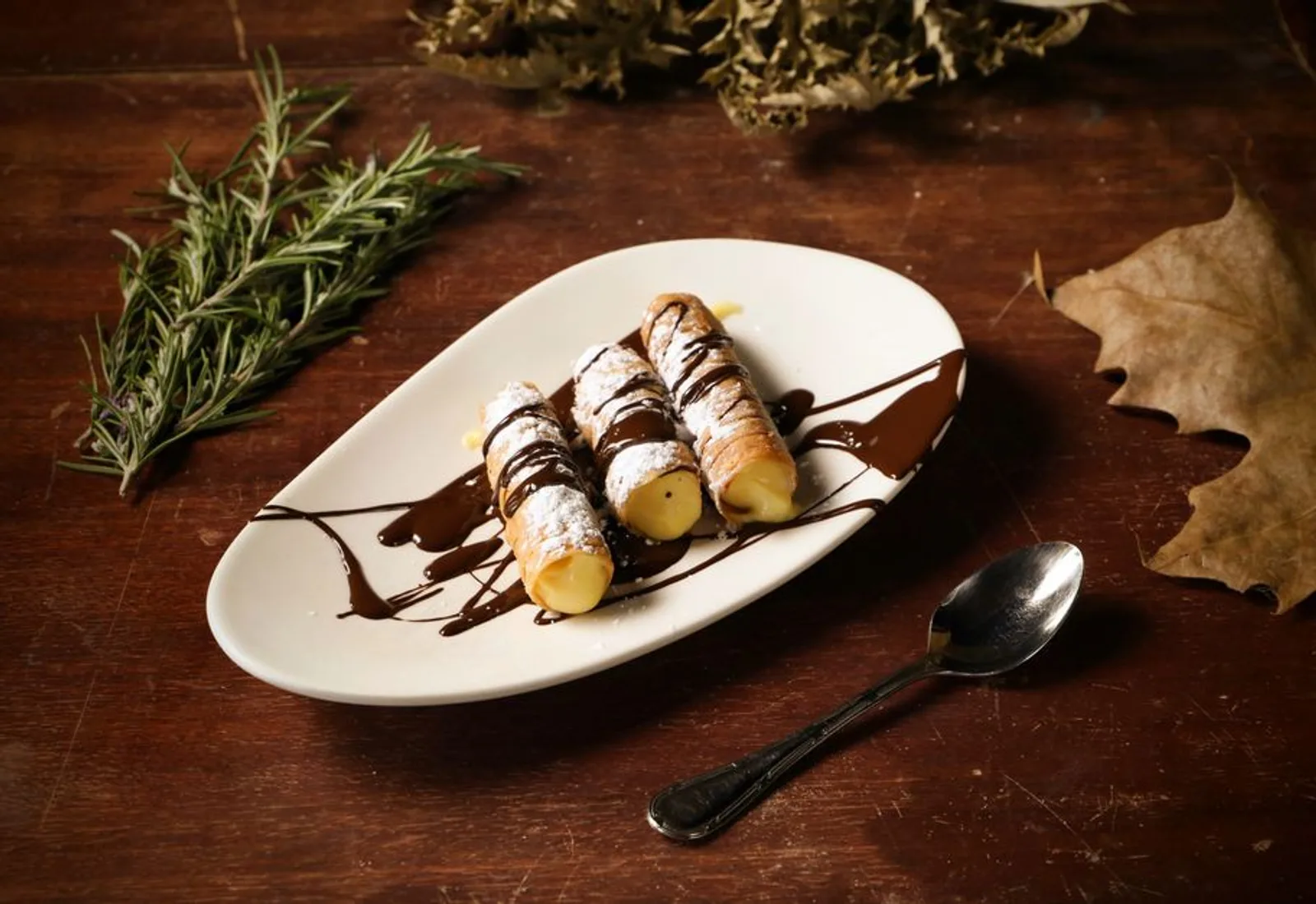 Two cannoli on a dark plate with a drizzle of chocolate