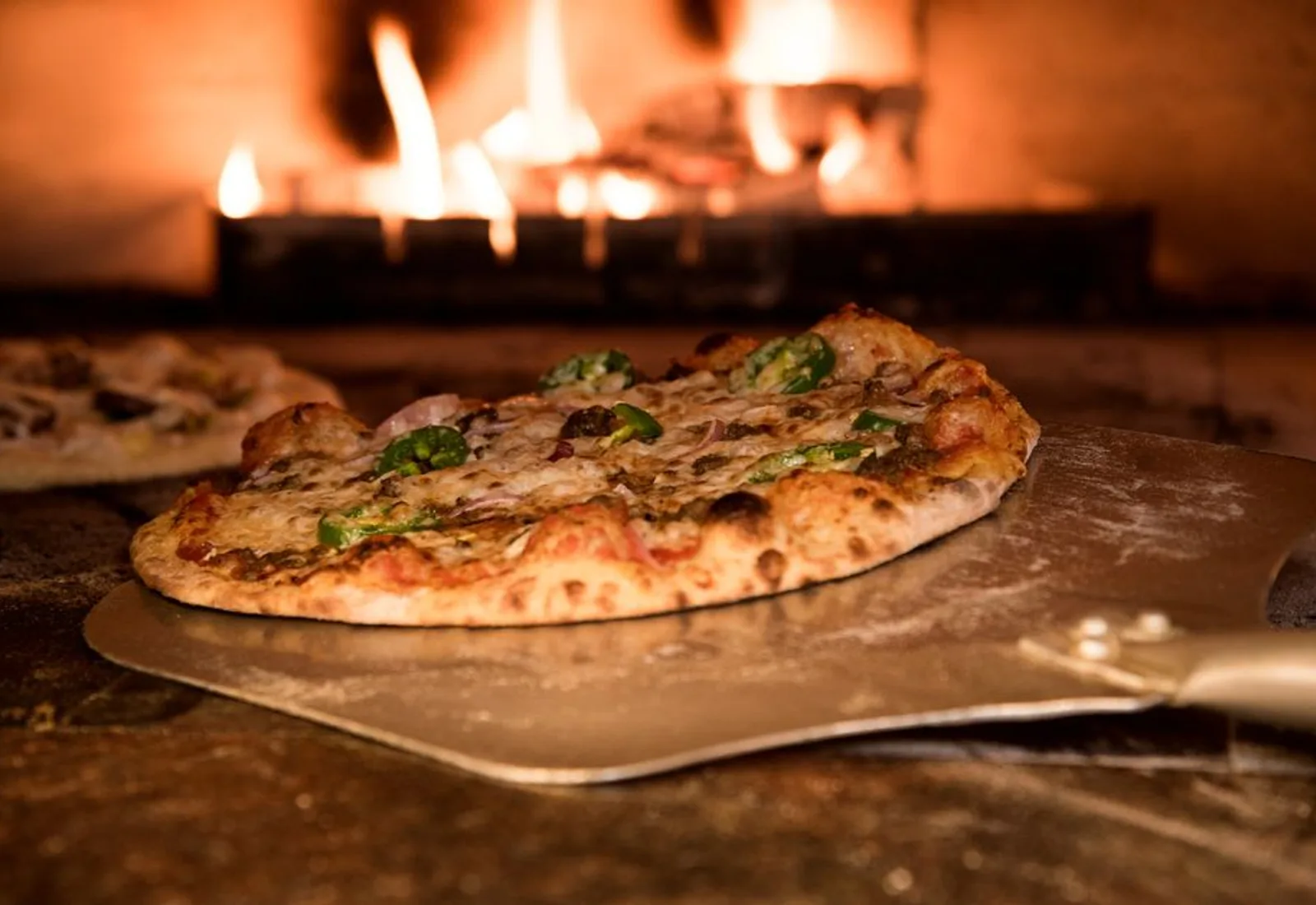 A blistered margherita pizza on a peel in front of the wood fire