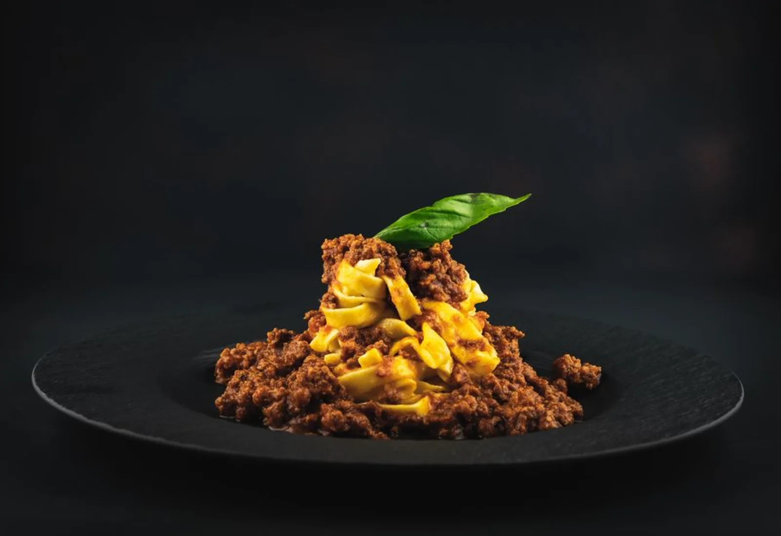 A bowl of fresh tagliatelle in a rich meat ragù on a wooden table