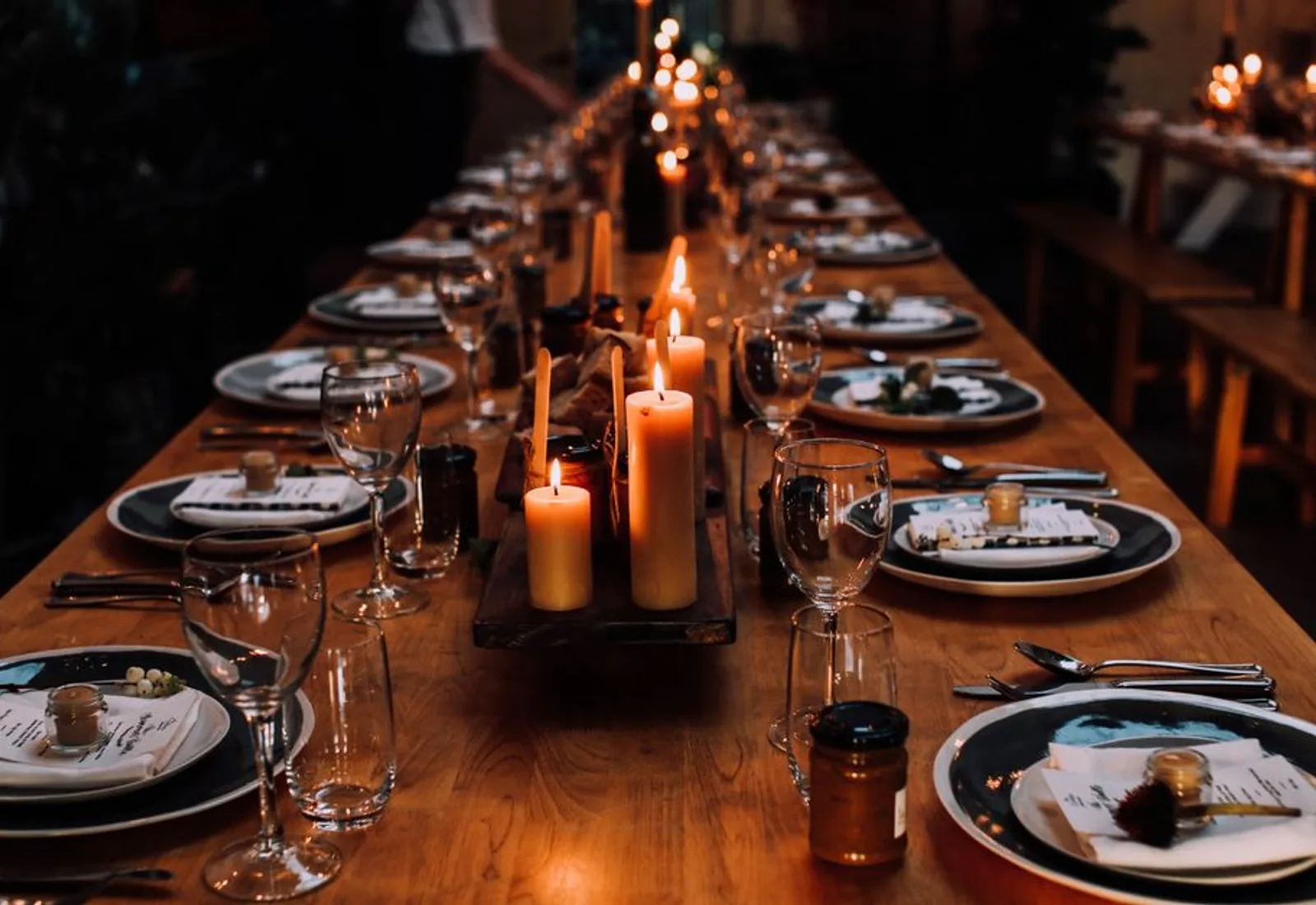 A long table set with candles down the middle, glowing in a dark dining room