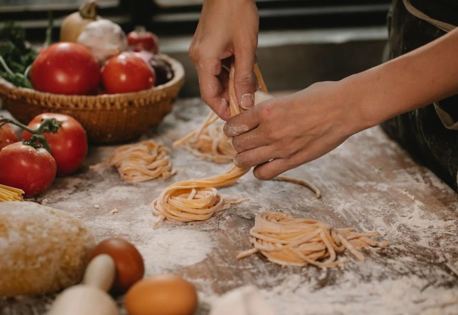 Hands cutting fresh tagliatelle into nests on a flour-dusted counter